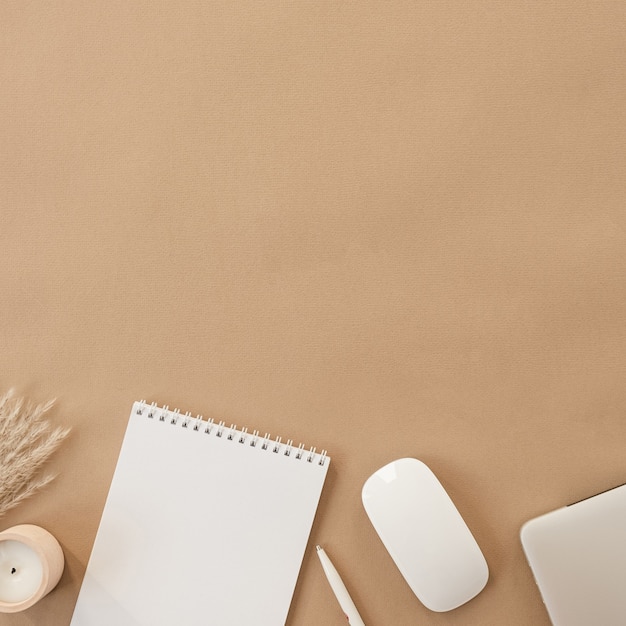 Flat lay of spiral flip notebook with blank paper sheet. Laptop, pampas grass, stationery on beige peachy pastel table. Top view