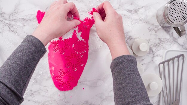 Flat lay. Step by step. Cutting out snowflakes with cookie cutters out of pink fondant on a marble counter.