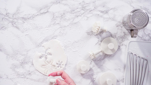 Flat lay. Step by step. Cutting out snowflakes with cookie cutters out of white fondant on a marble counter.