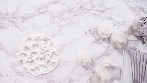 Flat lay. Step by step. Cutting out snowflakes with cookie cutters out of white fondant on a marble counter.