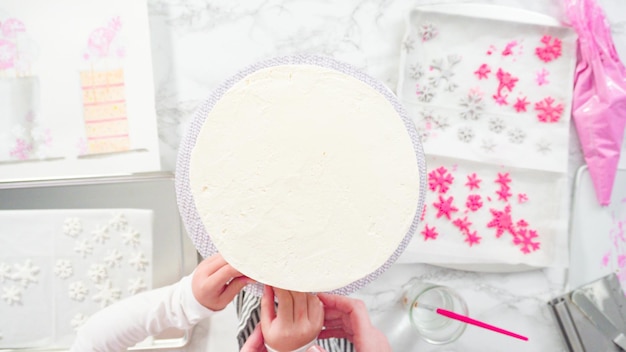 Flat lay. Step by step. Decorating round funfetti cake with pink and white fondant snowflakes.