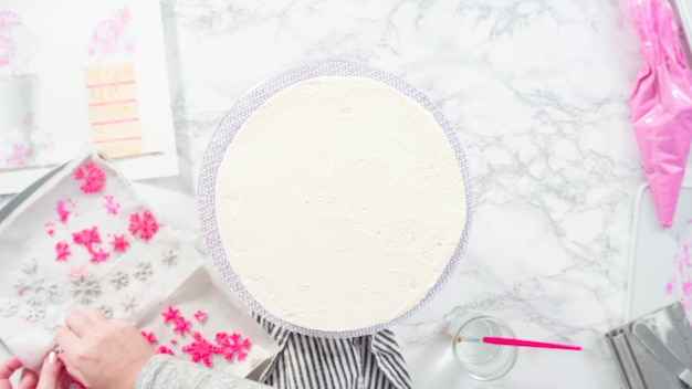 Flat lay. Step by step. Decorating round funfetti cake with pink and white fondant snowflakes.