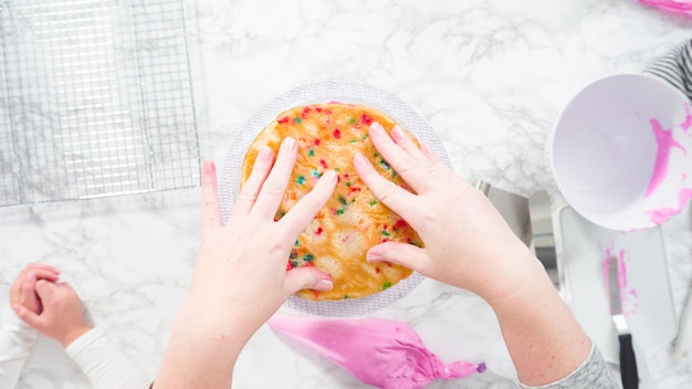 Flat lay. Step by step. Frosting round funfetti cake layers with pink buttercream frosting.