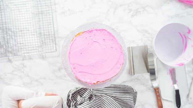 Flat lay. Step by step. Frosting round funfetti cake layers with pink buttercream frosting.