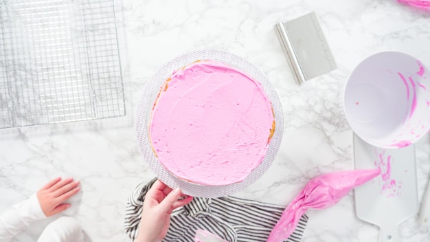 Flat lay. Step by step. Frosting round funfetti cake layers with pink buttercream frosting.