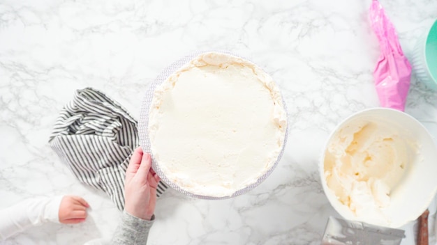 フラットレイ。ステップバイステップ。白いイタリアのバタークリームのフロスティングと丸いファンフェッティケーキのフロスティング。