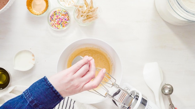 Flat lay. Step by step. Mixing ingredients together in a white mixing bowl to make unicorn chocolate cupcakes with buttercream frosting.