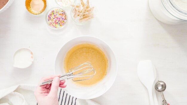 Flat lay. Step by step. Mixing ingredients together in a white mixing bowl to make unicorn chocolate cupcakes with buttercream frosting.