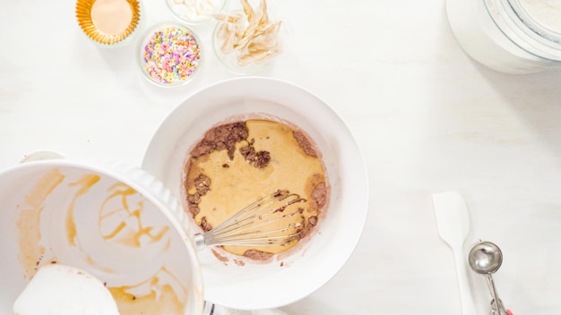 Flat lay. step by step. mixing ingredients together in a white mixing bowl to make unicorn chocolate cupcakes with buttercream frosting.