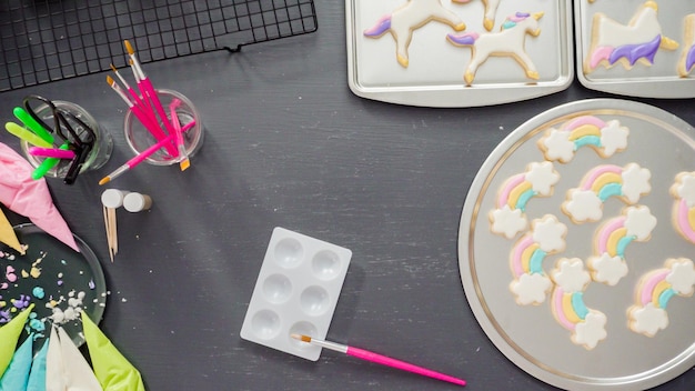 Flat lay. Step by step. Painting food glitter on top of unicorn sugar cookies with royal icing.