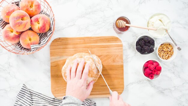 Flat lay. Step by step. Slicing a loaf of ciabatta bread with a bread knife on a wood cutting board.