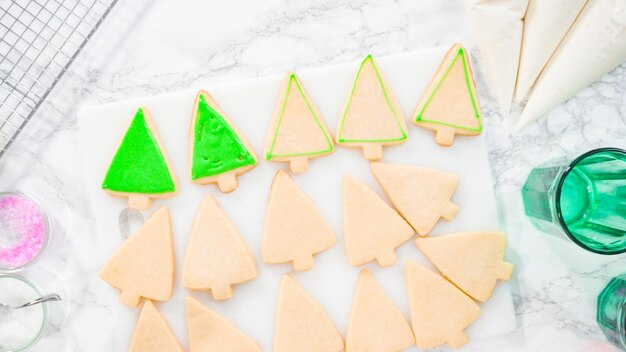 フラットレイ。ステップバイステップ。緑のロイヤルアイシングでクリスマスツリーの形をしたシュガークッキーをアイシングします。