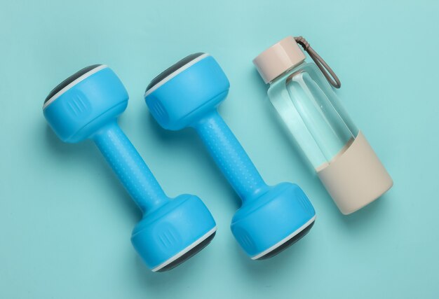 Flat lay style concept of healthy lifestyle, sport and fitness. Dumbbells, bottle of water on blue pastel background. Top view