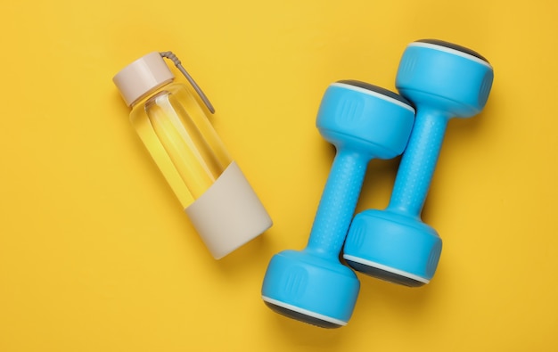 Flat lay style concept of healthy lifestyle, sport and fitness. Dumbbells, bottle of water on yellow background. Top view