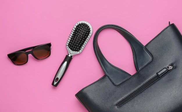 Flat lay style women's accessories on pink background. Bag, sunglasses, comb. Top view