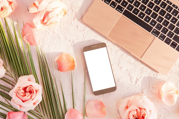 노트북, 휴대 전화와 세련 된 구성의 평면 배치. 그림자와 태양 빛 파스텔에 열 대 야 자 잎, 핑크 장미 꽃