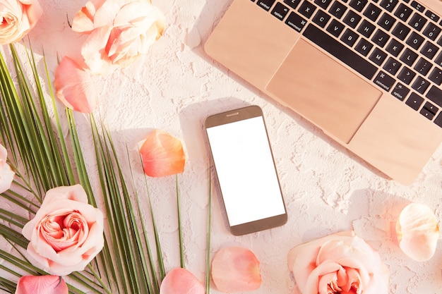 Flat lay of stylish composition with laptop, mobile phone. tropical palm leaf, pink rose flowers, on pastel with shadows and sun light