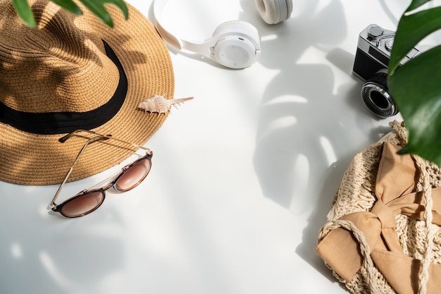 Flat lay of summer accessories with green tropical leaf and shadow on white desk.