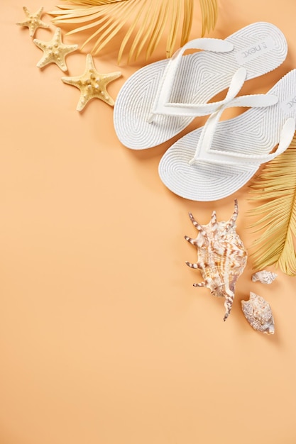 Flat lay summer composition Tropical palm leaves white flip flop seashells on pastel orabge background