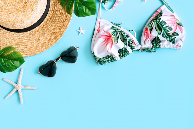 Flat lay of summer item with colorful bikini, beach hat, coral in starfish shape, sunglasses in heart shape and palm leaves