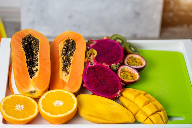 Flat lay of summer tropical fresh juicy fruits. Top view, vertical closeup shot of sliced papaya, mango, dragon fruit, passion fruit, orange on table. Selective focus.