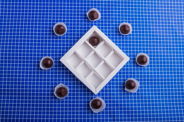Caramelle al cioccolato dolci piatte intorno alla scatola. sfondo blu a scacchi.