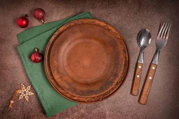 Flat lay of tableware set of empty plate on green napkin, spoon and fork, christmas baubles on table