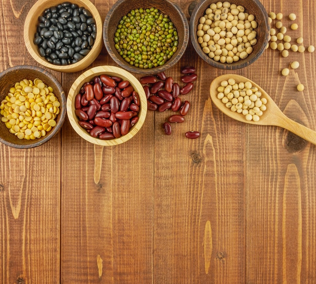 Flat lay, top view assorted beans including red bean, soybeans, black beans, mung beans on brown, beige wooden background