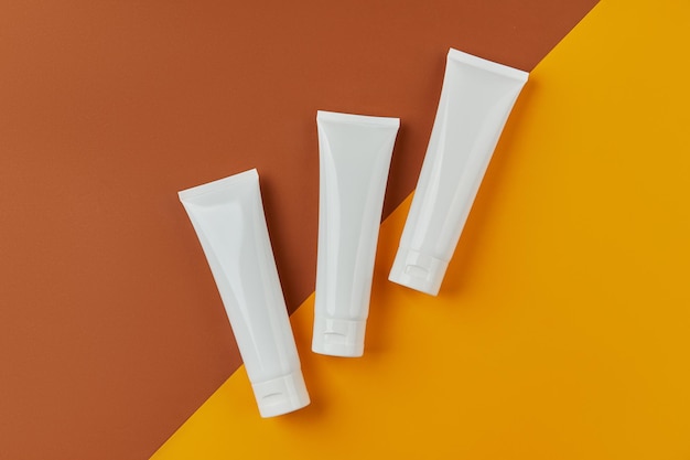 Flat lay top view blank white tubes bottles with skin care products on orange creative background