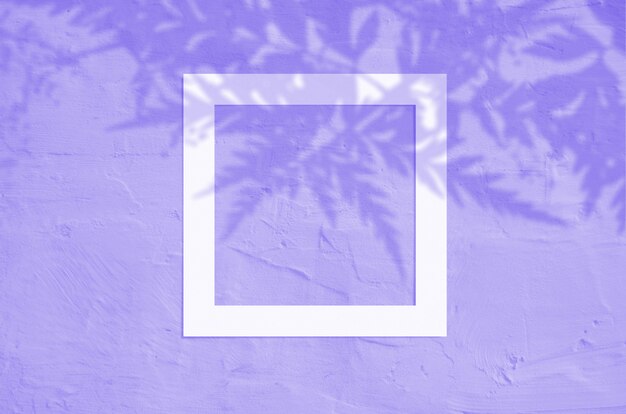 Flat lay top view of creative copyspace with paper frame and tropical leaves palm shadow on violet color background.