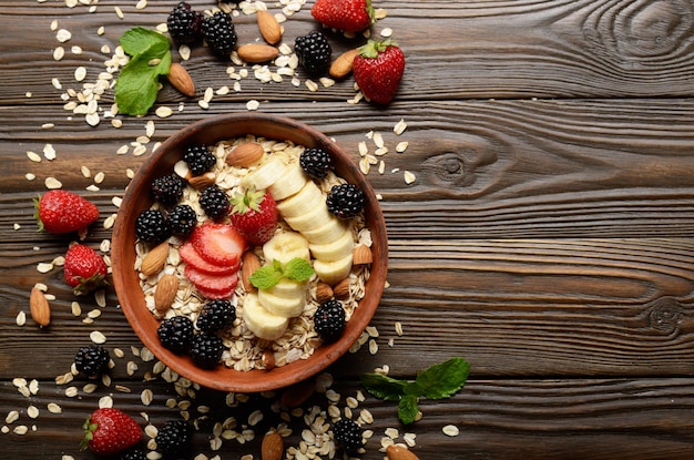 Flat lay top view at Fruit healthy muesli with banana strawberry almonds and blackberry in clay dish on wooden kitchen table