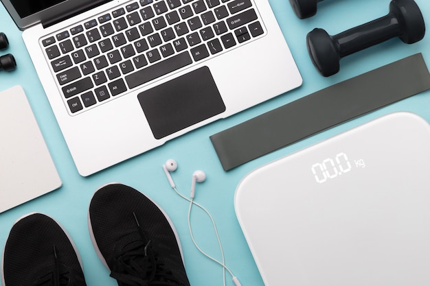 Flat lay top view of laptop with sport equipments on blue background.