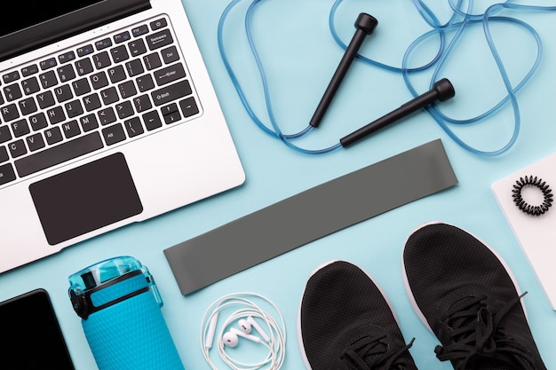 Flat lay top view of laptop with sport equipments on blue surface