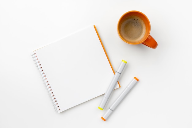 Flat lay top view notepad, markers and coffee cup on white table