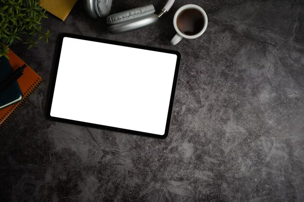 Фото Плоский вид сверху на цифровой планшет с пустым дисплеем, кофейной чашкой, наушниками и блокнотами на мраморном столе