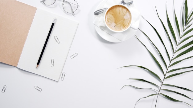 Flat lay, top view office table desk. Workspace with blank clip board, office supplies, pencil, green leaf, and coffee