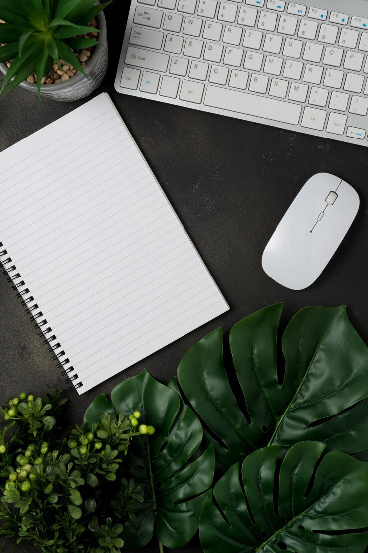 Flat lay top view office table desk Workspace with blank notebook keyboard office supplies and green leaves on black background