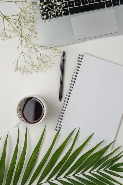 Flat lay top view office table desk Workspace with blank notebook office supplies green leaf and coffee cup on white background