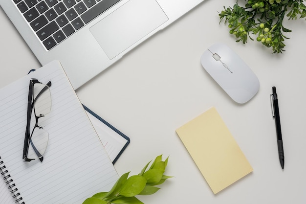 Flat lay top view office table desk Workspace with blank notebook office supplies green leaves and eyeglasses on white background