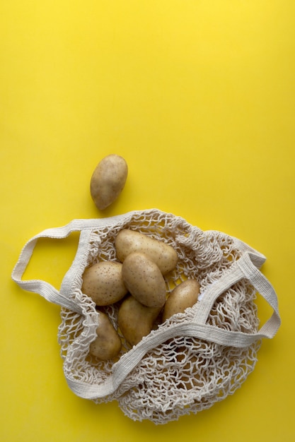 Flat lay top view raw organic potatoes in string bag on yellow background