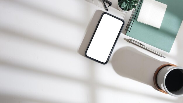 Flat lay top view of smart phone notebook and coffee cup on white table Copy space for your text