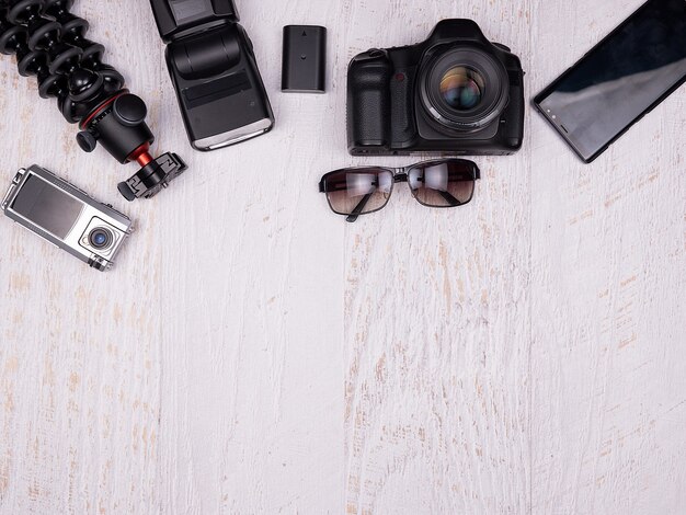 Flat lay top view of traveler accessories on white wooden background. DSLR and action camera, tripod, flash, smartphone