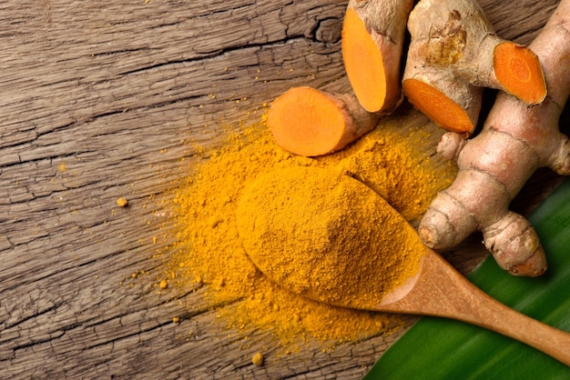 Flat lay (top view) of Turmeric (curcumin) powder in wooden spoon with fresh rhizome on wood background.