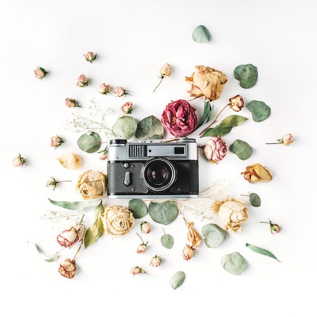 Flat lay, top view vintage retro photo camera, beige roses and green leaves