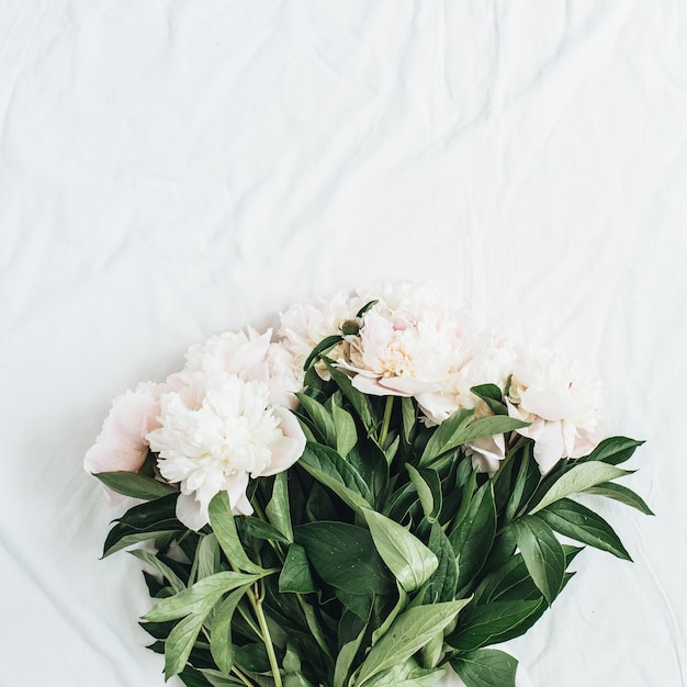 Flat lay, top view of white peonies flower bouquet on white blanket surface