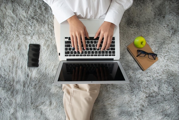 Flat lay top view of young woman sitting on carpet and using laptop for online learning.