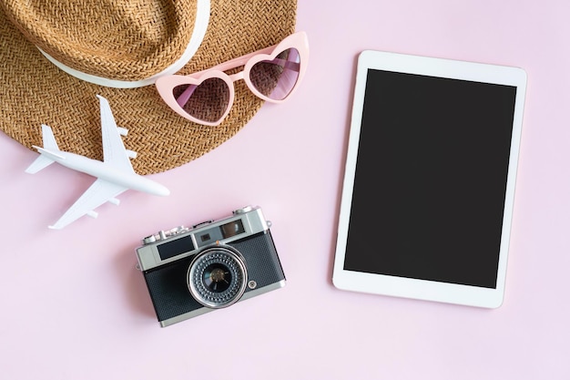 Flat lay of travel items and tablet on pink desk Summer holiday and planning a trip concepts Top view and copy space