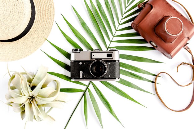 Flat lay traveler accessories on white background with retro camera straw hat sunglasses and tropical palm leaf Travel concept background