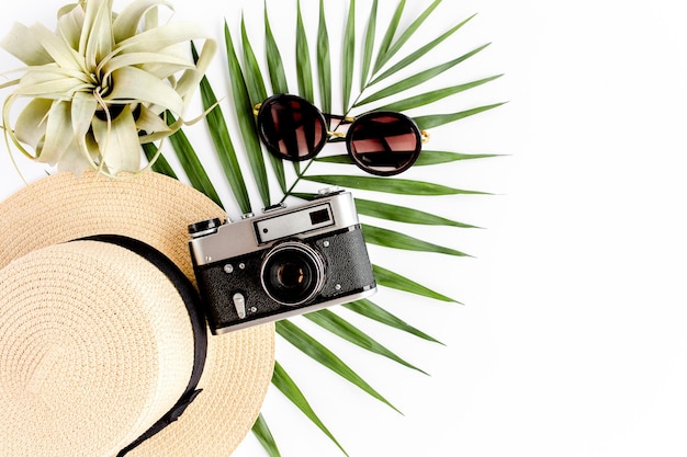 Flat lay traveler accessories on white background with retro camera straw hat sunglasses and tropical palm leaf Travel concept background