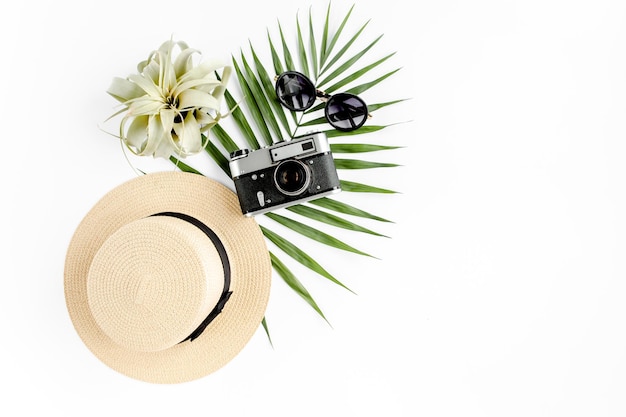 Flat lay traveler accessories on white background with retro camera straw hat sunglasses and tropical palm leaf Travel concept background